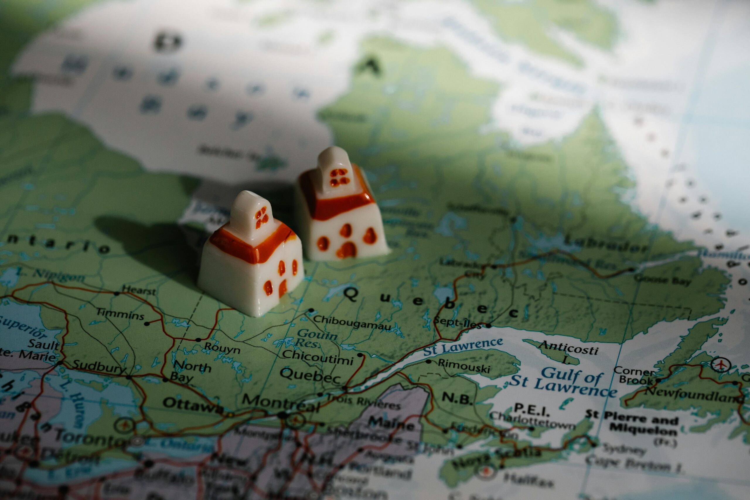 Close-up view of two miniature house figurines placed on a map of Quebec, Canada.